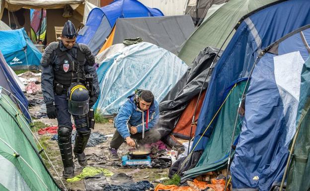 Agente de policía francés andando entre las tiendas de campaña de un campamento de refugiados.