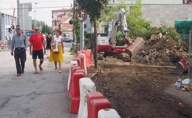 Un grupo de vecinos camina por la calzada, junto al paso a nivel de FEVE, mientras se ejecutan las obras