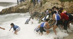 Los remeros de Santander, ayudados por el público, intentan sacar la trainera de las rocas. / SANE/